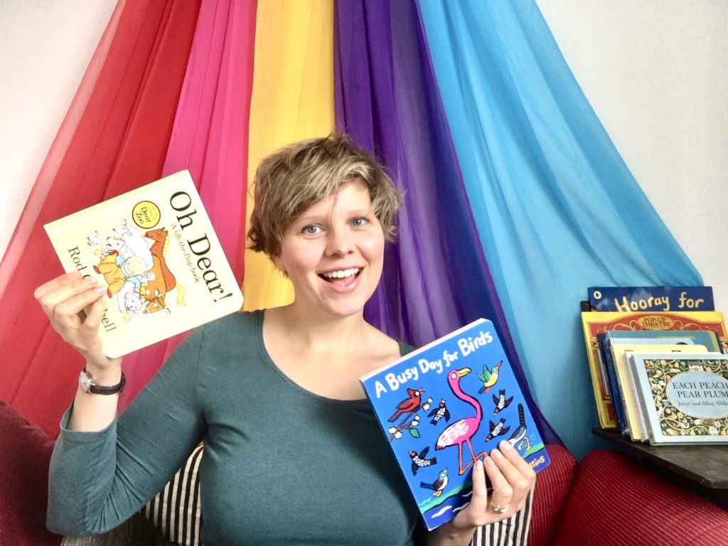 A smiling presenter holds up children's books